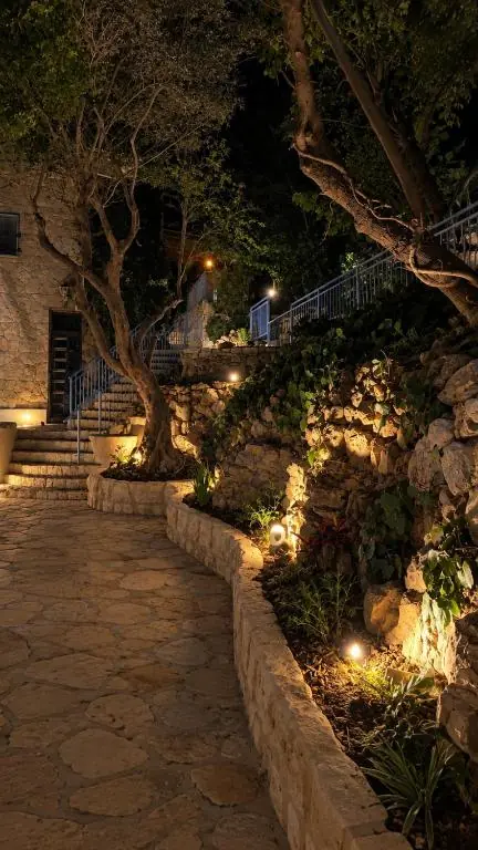 שביל האבן בגן בלילה, מואר בין עצי הזית, ומדרגות האבן העולות אל הבית